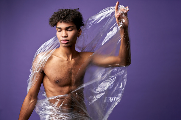 Portret młodego mężczyzny łamie plastikową torbę dłońmi sportowca. Latynoski transgenderowy mężczyzna zamknięte oczy - Zdjęcie, obraz