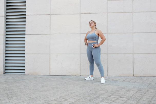 Pretty fit young plus size woman in sports bra and leggings standing outdoors after jogging - Foto, Imagem