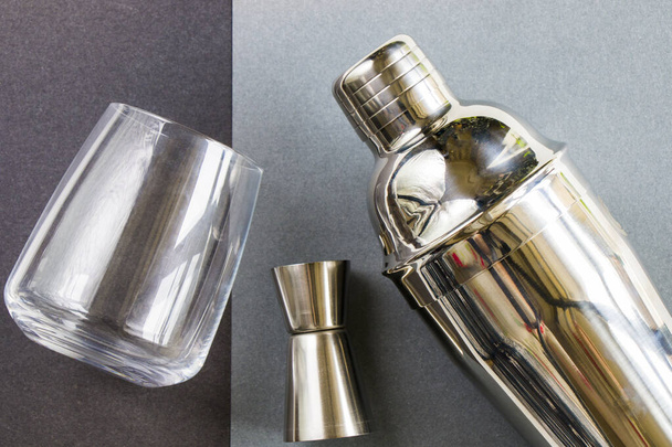 A top view of a barmen's tools on a gray background - Metal shaker with a cocktail glass beside it - Foto, imagen