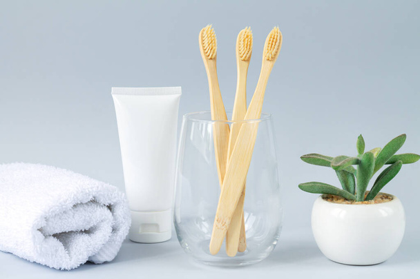 Vaso con conjunto familiar de cepillos de dientes de bambú eco biodegradables junto a pasta de dientes, toalla y planta verde - Foto, Imagen