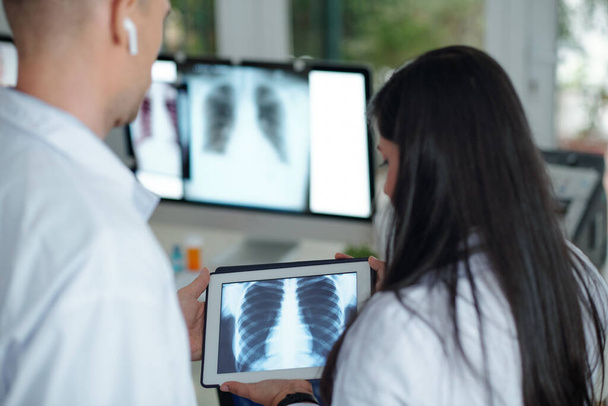 Хирурги обсуждают рентген грудной клетки пациента с опухолью на планшетном компьютере, вид сзади - Фото, изображение