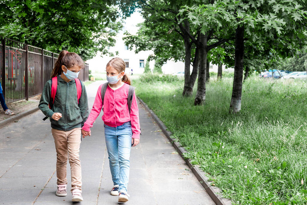 Dos niñas que usan mascarilla protectora y regresan a la escuela durante la pandemia de coronavirus. - Foto, Imagen