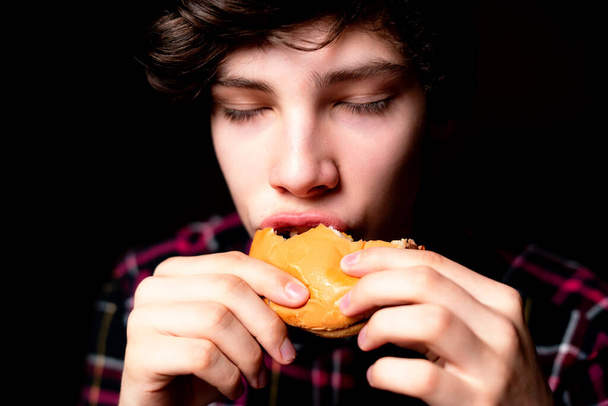 close-up foto van mond beet junk hamburger op donkere achtergrond geïsoleerd b - Foto, afbeelding