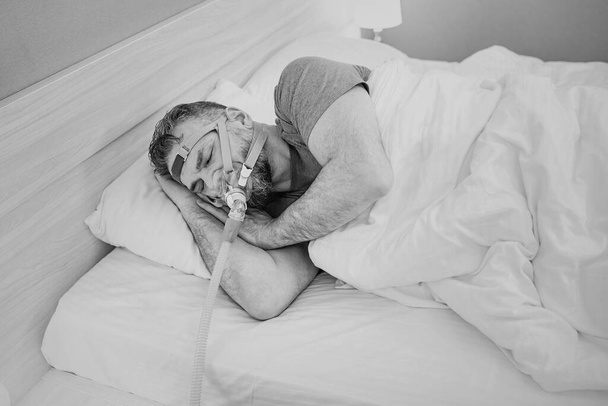 Monokróm portré alvó ember krónikus légzési problémák fontolgatja a CPAP gép az ágyban. Egészségügyi, Obstruktív alvási apnoe terápia, CPAP, horkolás koncepció - Fotó, kép