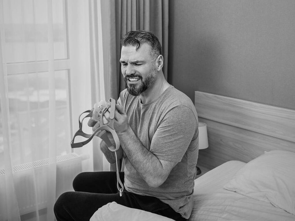 monochromatyczny portret szczęśliwego wypoczętego mężczyzny z chronicznymi problemami z oddychaniem po użyciu maszyny CPAP siedzącej na łóżku w sypialni. Opieka zdrowotna, CPAP, Obturacyjna terapia bezdechu sennego, koncepcja chrapania - Zdjęcie, obraz