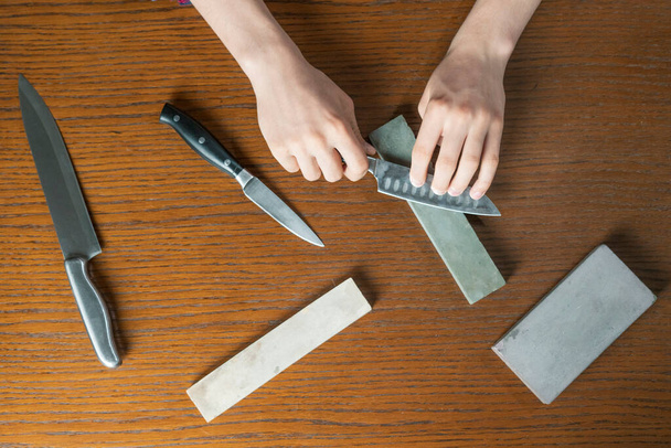 junger Mann schärft Messer auf Holztisch auf dunklem Hintergrund - Foto, Bild