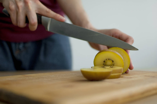 Female hands is cutting a fresh ripe golden kiwi fruit on a cut wooden board. Exotic fruits, healthy eating concept - Foto, imagen