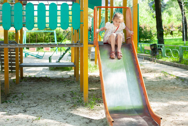 A menina está a brincar no parque. A criança desliza para baixo do slide das crianças. - Foto, Imagem