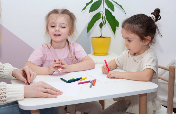 Mladý učitel ze školky kreslí s dětmi. Máma a dcery kreslí tužkami u stolu. - Fotografie, Obrázek