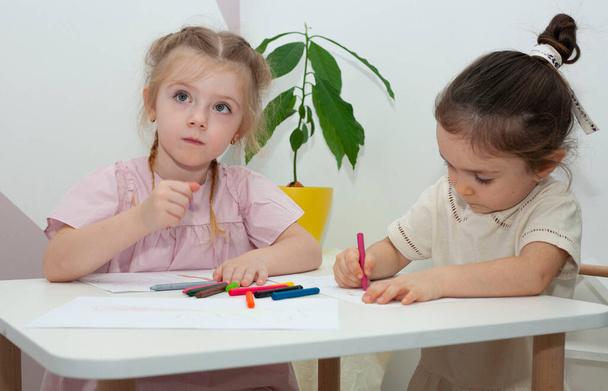 Молодий учитель дитячого садка малює з дітьми. Мама з доньками малюють олівцями за столом.. - Фото, зображення