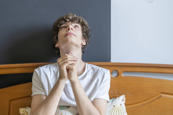 joven está rezando en la cama en casa contra la ventana b - Foto, Imagen