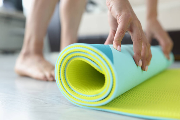 Woman folds yoga or fitness mat after workout at home in living room - Φωτογραφία, εικόνα