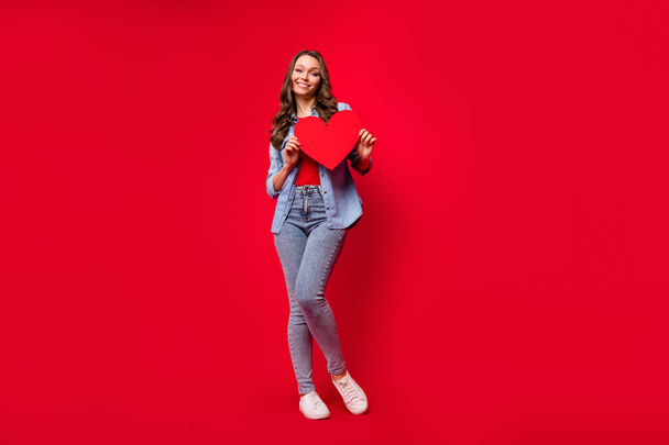 Full length body size photo of girl keeping red heart shaped card on date isolated on vibrant red color background with copyspace - Fotó, kép