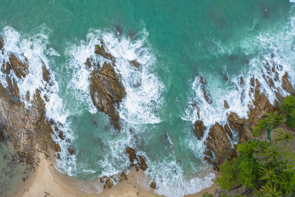 Aerial top view of white waves in green sea hit on the large rocks in summer day. - Photo, Image