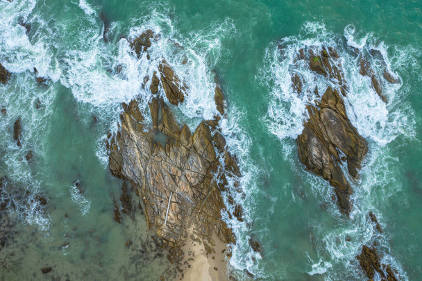 Bovenaanzicht vanuit de lucht van witte golven in groene zee getroffen op de grote rotsen in de zomerdag. - Foto, afbeelding