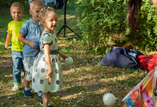 Les jeunes enfants participent à une compétition lors d'une fête d'enfants. Garçons et filles jouent dans le jardin. Les enfants jettent la balle dans le panier. Fête d'anniversaire. - Photo, image