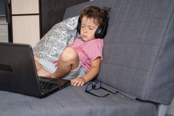 Cute caucasian boy sleep while using laptop with glasses and headphones studying at home - Foto, afbeelding