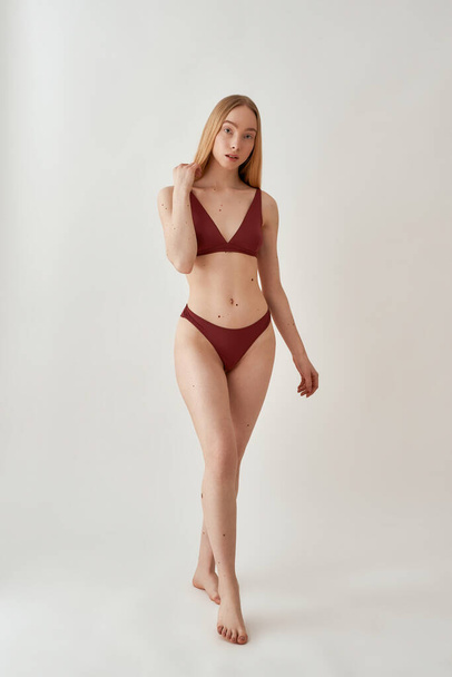 Full length shot of attractive young slim caucasian woman with fit body wearing burgundy underwear looking at camera, posing isolated over light gray background - Fotoğraf, Görsel