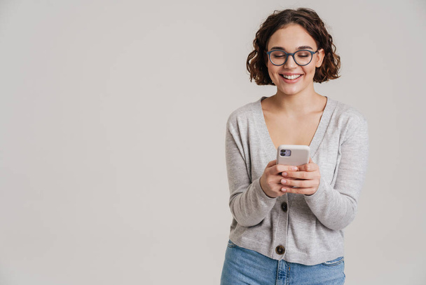 Portrait of an attractive happy young girl in casual clothes using mobile phone isolated over white background - Φωτογραφία, εικόνα