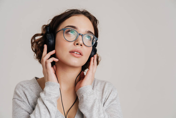 Lovely young woman listening to music with headphones isolated over white background - 写真・画像