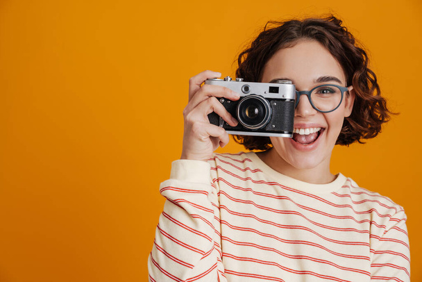Cheerful young woman taking photos with camera isolated over yellow background - Фото, зображення