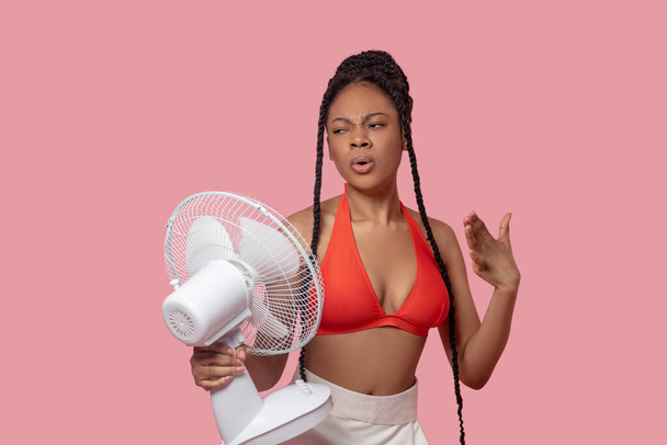 Smiling african american woman holding a fan looking tired from heat - Фото, зображення