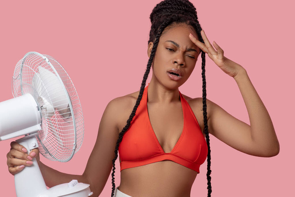 Smiling african american woman holding a fan looking tired from heat - Zdjęcie, obraz