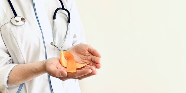 Ruban orange dans les mains d'un médecin. sclérose en plaques, concept de sensibilisation à l'oncologie. Place pour votre texte. - Photo, image
