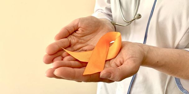 Orangefarbenes Band in den Händen eines Arztes. Multiple Sklerose, onkologisches Aufklärungskonzept.  - Foto, Bild