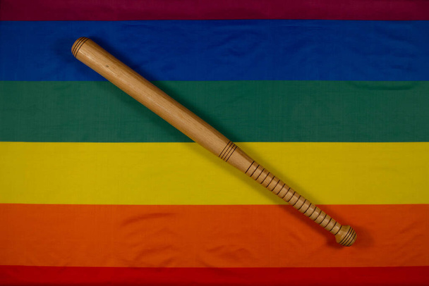 Baseballschläger aus Holz mit originellem Design auf Hintergrund der LGBT-Regenbogenflagge. Das Symbol der Liebe und Toleranz gegen das Symbol des Hasses und der Intoleranz. Monat des LGBT-Stolzes. Nahaufnahme. Ansicht von oben - Foto, Bild