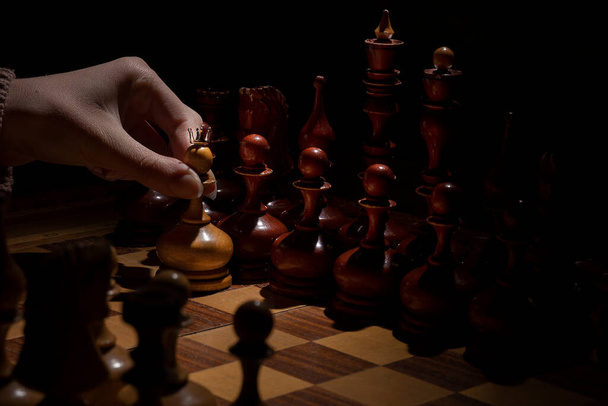 female hand holds a pawn with a crown on a dark background. old chess. business concept. - Foto, afbeelding