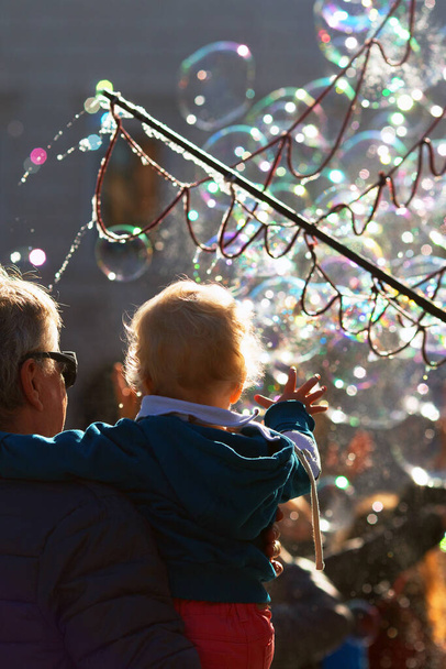Malá holčička sleduje světlé mýdlové bubliny výkon spolu se svým dědečkem. Svislý formát - Fotografie, Obrázek