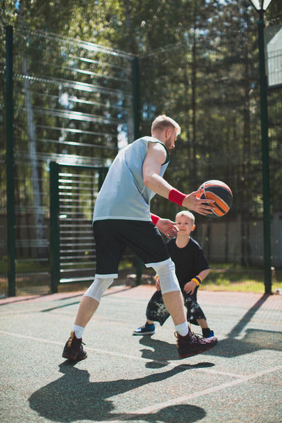 American athletes trainer and little boy kid playing basketball outdoors. Basketball athlete training on court - Zdjęcie, obraz