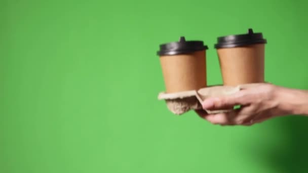Hands holding two cups brown paper with black lid. Two coffee special offer or promo. Hands holding two cups on green background. Tea or Coffee to go. Brown paper cup with black lid. - Footage, Video