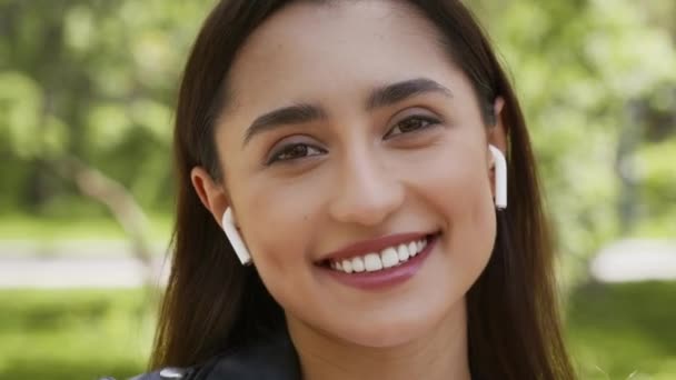 Mujer joven positiva con auriculares escuchando música en el parque - Metraje, vídeo