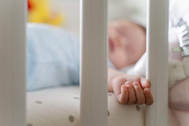 Top view on small infant baby boy lying in cradle bed at home in day sleeping - childhood parenthood and growing up concept selective focus on hand - Valokuva, kuva