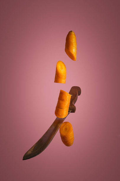 Floating knife slicing carrot. Gray background. Creative food concept - 写真・画像