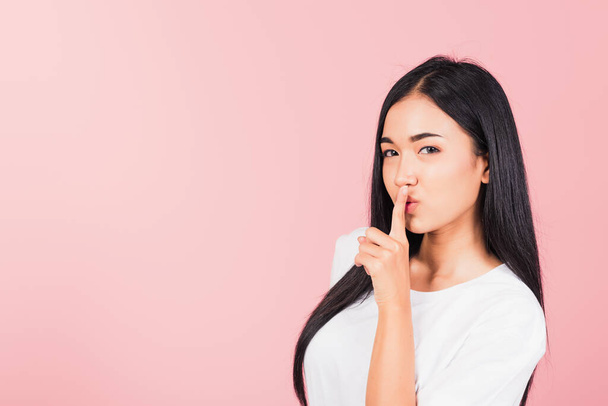 Asian happy portrait beautiful cute young woman smile stand making finger on lips mouth silent quiet gesture studio shot isolated on pink background, Thai female looking to camera away with copy space - Photo, Image
