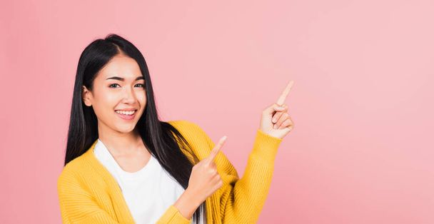 Asian happy portrait beautiful cute young woman standing makes gesture two fingers point upwards above presenting product something, studio shot isolated on pink background with copy space - Foto, immagini