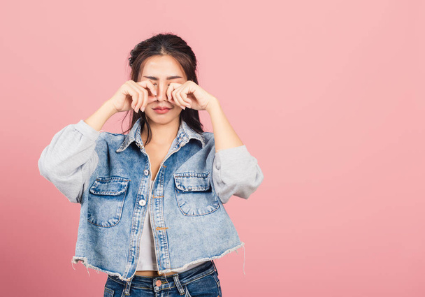 Asian portrait beautiful cute young woman wear denim bad mood her cry wipe tears with fingers, studio shot isolated on pink background, Thai female feeling sad unhappy crying with copy space - Foto, Imagen