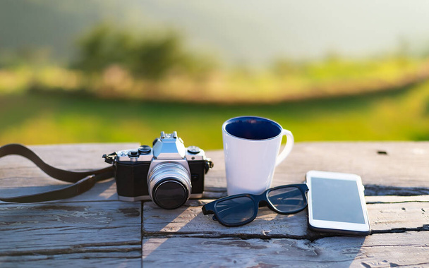 Cup with tea on table over mountains landscape with sunlight vintage. Beauty nature background  of coffee next to old photo camera on a wooden table.  - Zdjęcie, obraz