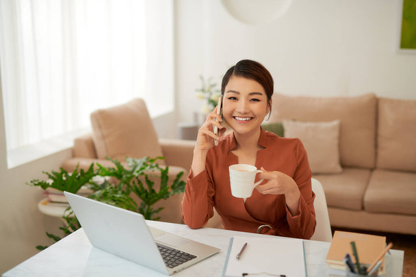 Muotokuva hymyilevä nuori nainen käyttää kannettavaa tietokonetta ja puhuu matkapuhelimella - Valokuva, kuva