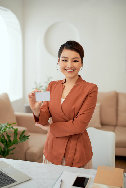 Portrait of businesswoman holding name card while stand in office room - Photo, Image