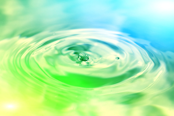 Water drop falling in colorful water - Photo, Image