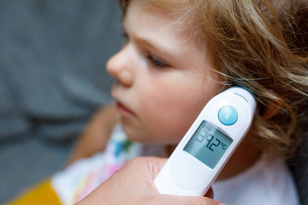 Matka mierzy temperaturę dla swojej małej przedszkolanki, chore dziecko z termometrem na podczerwień w domu, gorączka wysokiej jakości Matka trzyma cyfrowy termometr na podczerwień. - Zdjęcie, obraz