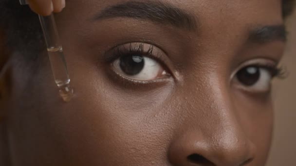 Schwarze Frau bei der Anwendung von Gesichtsserum mit Tropfer, beigem Hintergrund, Nahaufnahme - Filmmaterial, Video