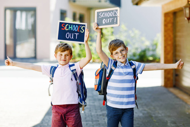 Two little kid boys with backpack or satchel. Schoolkids on the way to school. Healthy children, brothers and best friends outdoors on street leaving home. Schools out on chalk desk. Happy siblings. - Photo, Image