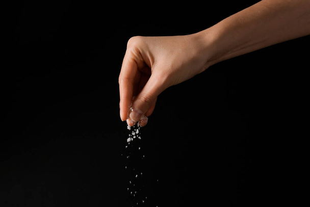 Woman sprinkling salt on dark background, closeup - Foto, Imagem