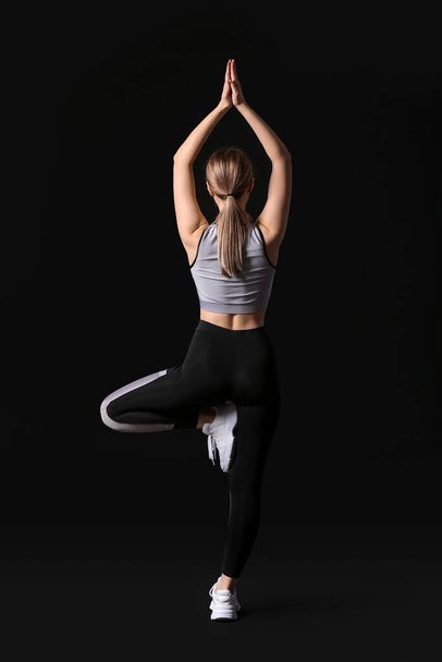 Sporty young woman doing yoga on dark background - Fotó, kép