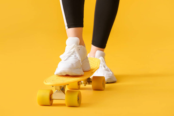 Sporty young woman with skateboard on color background, closeup - Фото, зображення